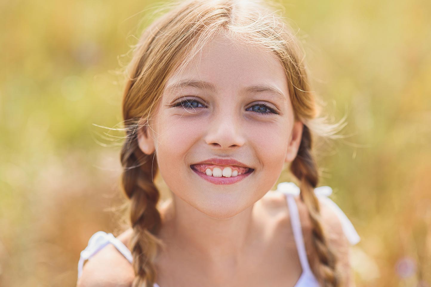 A pediatric dental patient with ClearCorrect aligners smiles happily outdoors on a sunny day.